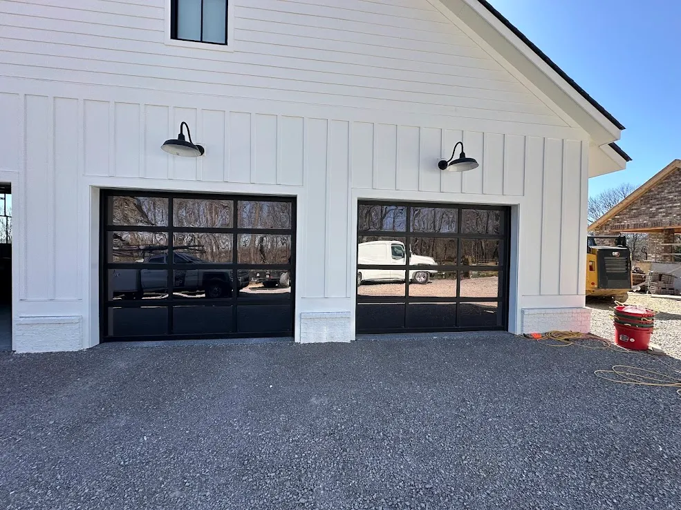 Two black full-view glass garage doors on a white board-and-batten garage