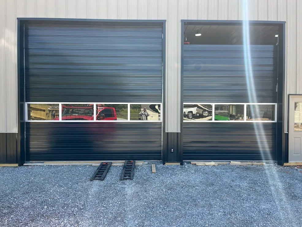Two black insulated shop doors with a row of glass lites, closed on a gravel apron
