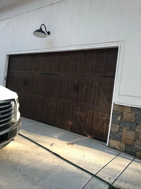A brown wood-look garage door closed beside a parked truck, shot from the side