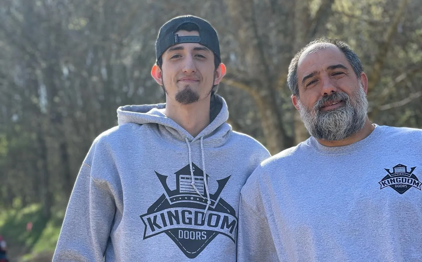 Clay Caro and his father Chad Caro outdoors in gray Kingdom Doors hoodies