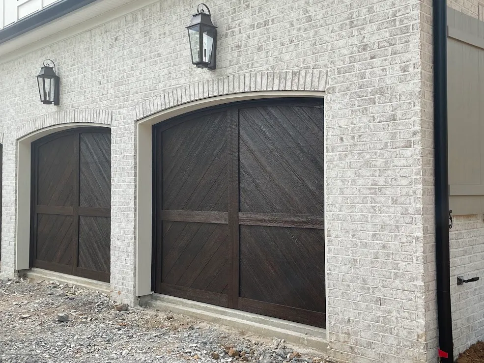 Two dark arched garage doors with black strap hinges in white-painted brick