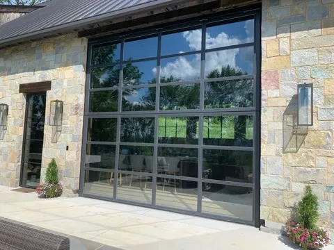A tall full-view glass garage door with black frames set into a stone house