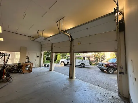 A sectional door rolled up on its tracks, seen from inside the garage, a truck parked in the drive