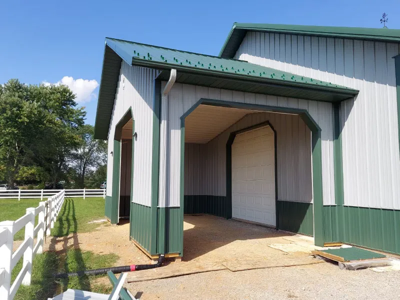 A tall white roll-up door in a gray pole barn with green trim, framed in an open bay