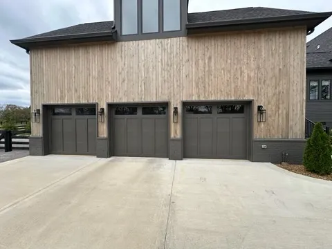 Three gray carriage doors under a tall cedar-clad gable