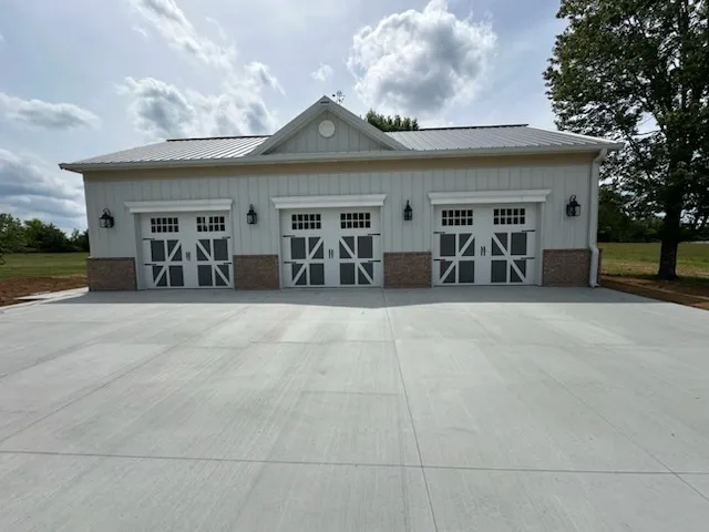 Three white carriage-style garage doors with X-brace panels and windows on a white ranch house