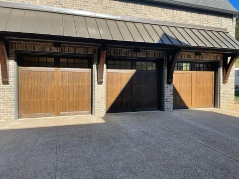 Three stained wood carriage doors with rows of windows under a standing-seam metal awning, set in brick