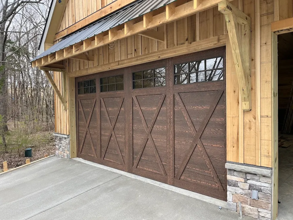 A stained walnut X-brace carriage door with a row of windows, set in cedar and stacked stone
