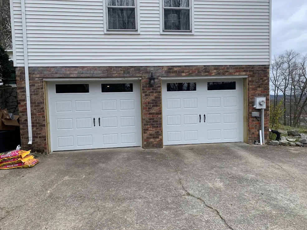 Two white carriage-style doors with black handles set into a brick garage